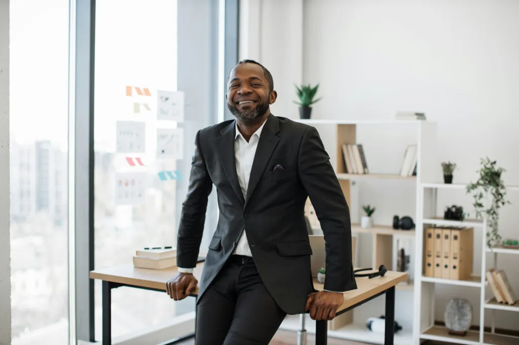 Company leader resting on edge of office desk