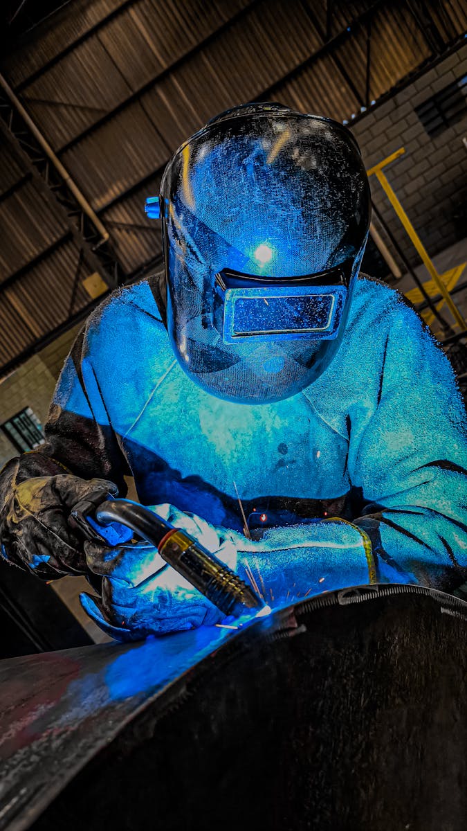 A welder in blue welding in a dark room